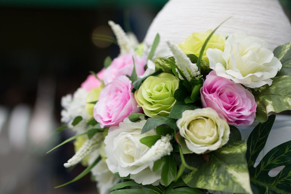 A floral arrangement featuring a bouquet of fresh roses and peonies in pastel shades of pink, white, and light green, accented with sprigs of white veronica and lush green foliage. The flowers are arr
